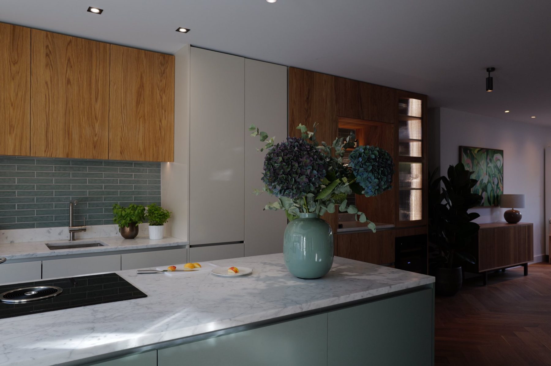 A kitchen designed by F*HD, with hydrangeas in a green vase on a marble island and a herringbone floor leading to the living room